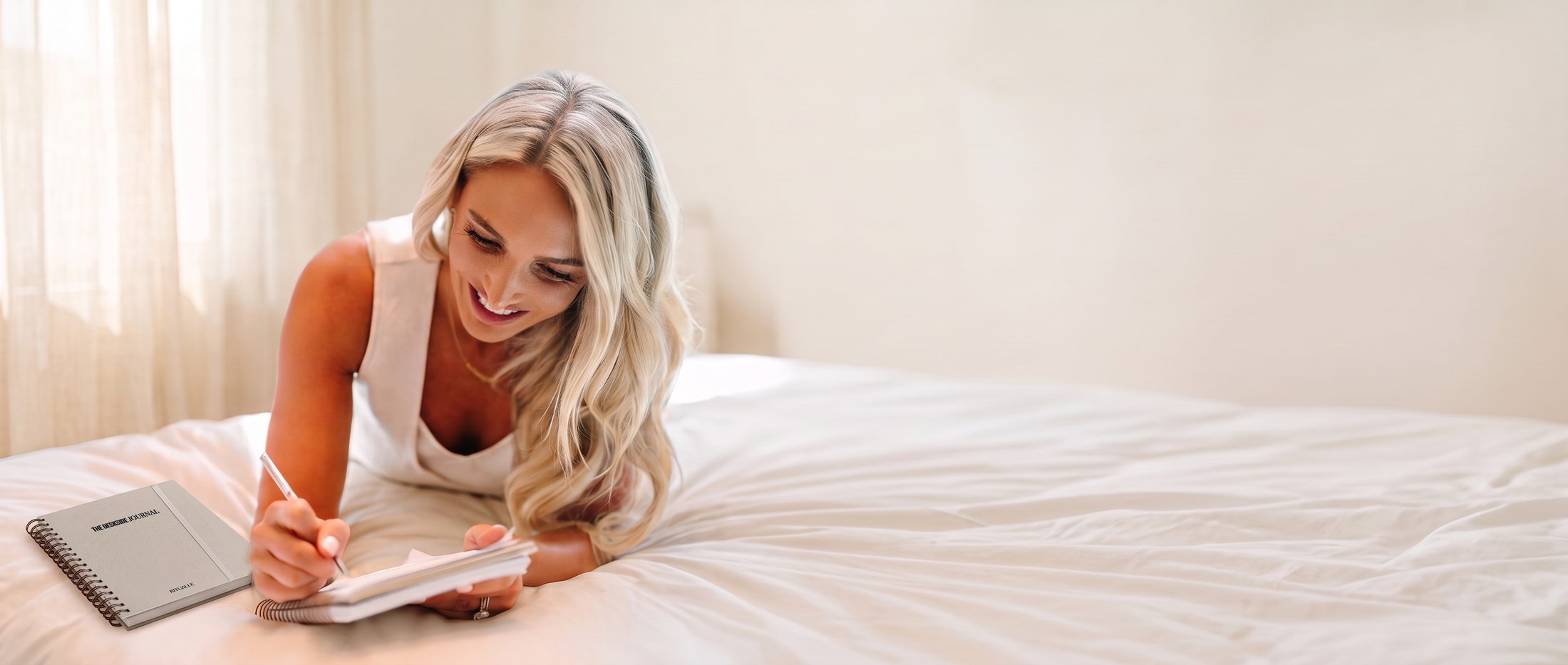 Alex Payetta writing in her Bedside Journal on her bed, the Deskside Journal beside her