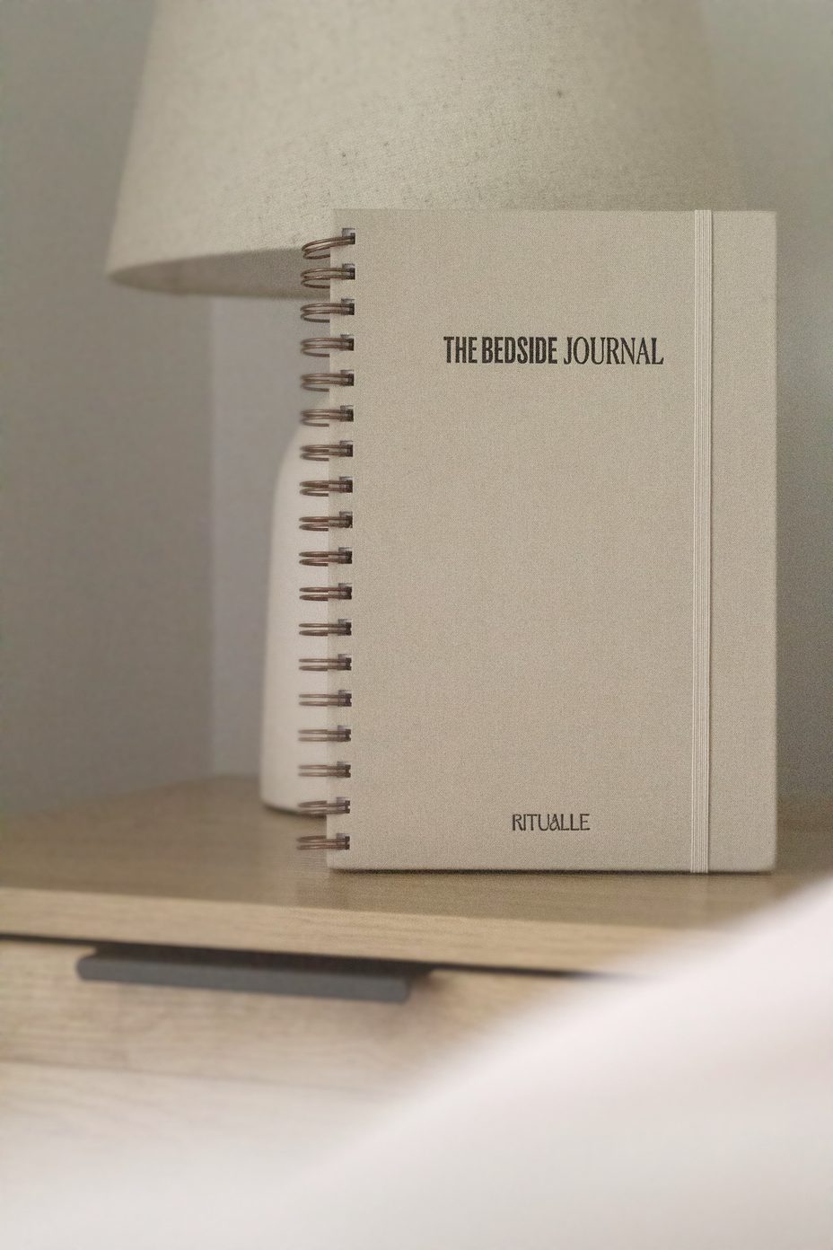 The Bedside Journal on a nightstand by a lamp